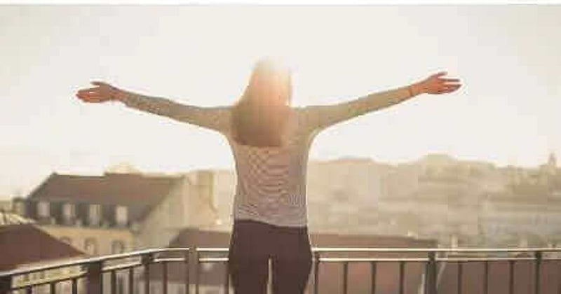 Person standing outdoors with arms outstretched at sunrise, illustrating optimism and longevity research